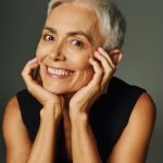 portrait of joyful senior lady with short silver hair looking at camera on grey, elegance and charm